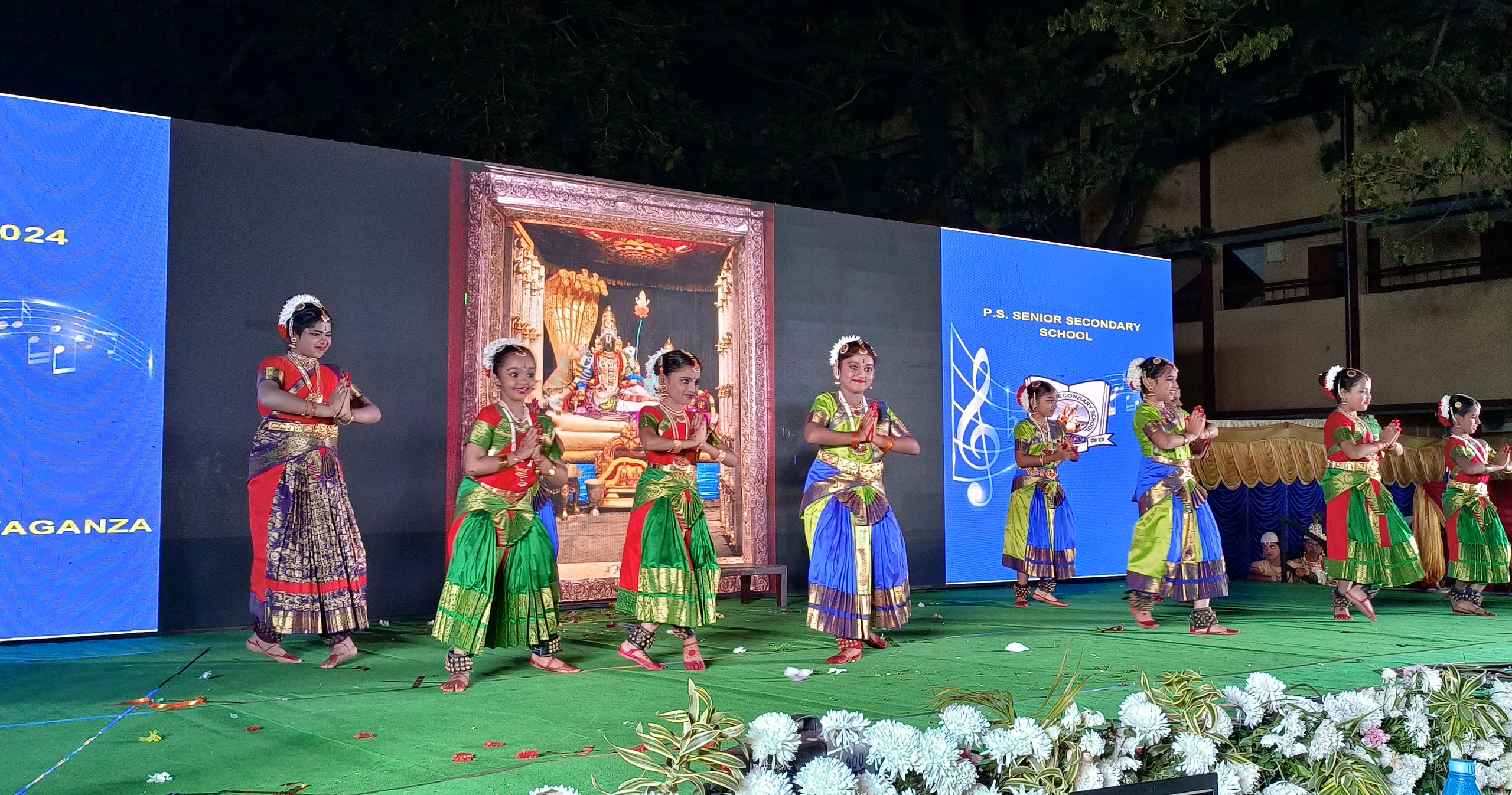 A row of students in classical dance costume performing on a stage decorated with flowers