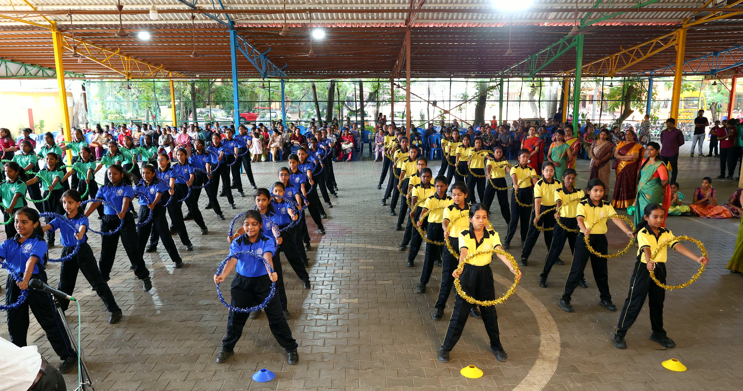 Rows of students in blue, green and yellow kits performing a hoop drill in the covered sports hall